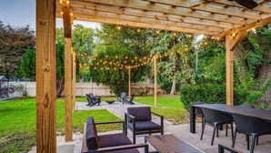 An outdoor patio with wooden pergola, string lights, and seating arrangements. - Upscale 6BR Home w/ Office (Clinton Township)