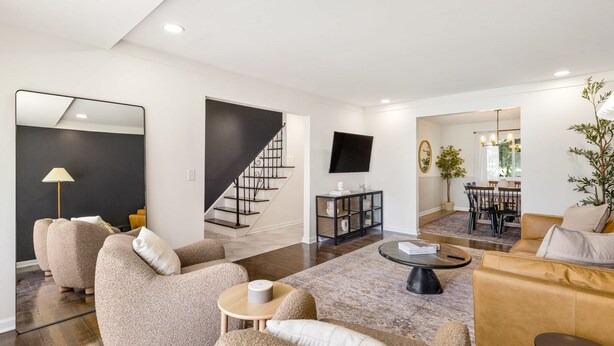 A modern living room with a sofa, coffee table, and a staircase leading to a dining area. - Upscale 6BR Home w/ Office (Clinton Township)