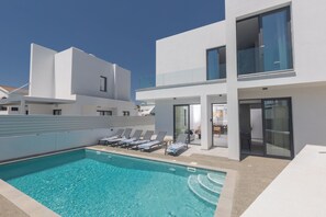 A modern poolside area with a clear blue pool, lounge chairs, and a contemporary building with large windows.