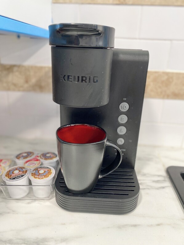 A Keurig coffee maker with a red mug on its drip tray, a stack of coffee pods, and a kitchen counter.