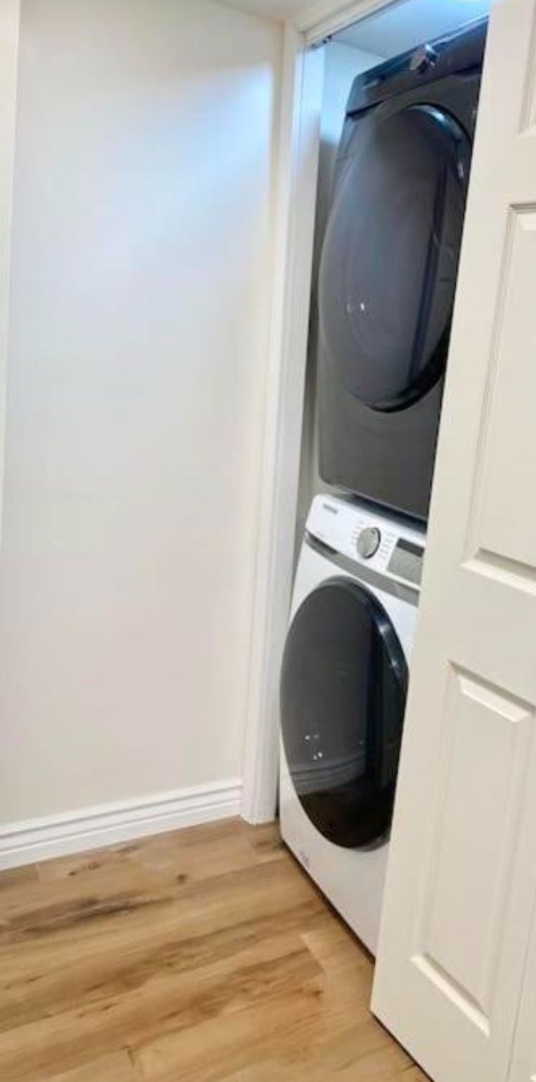 Une buanderie équipée d’un lave-linge et d’un sèche-linge superposés, avec un plancher en bois et des murs blancs.
