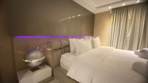 Een moderne hotelkamer met een groot bed, een nachtkastje met lamp en een hoofdeinde met ingebouwde verlichting.