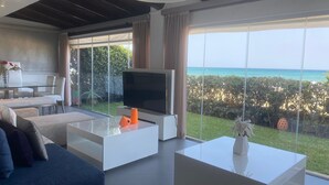 Een moderne woonkamer met een grote televisie, witte banken en uitzicht op de oceaan.