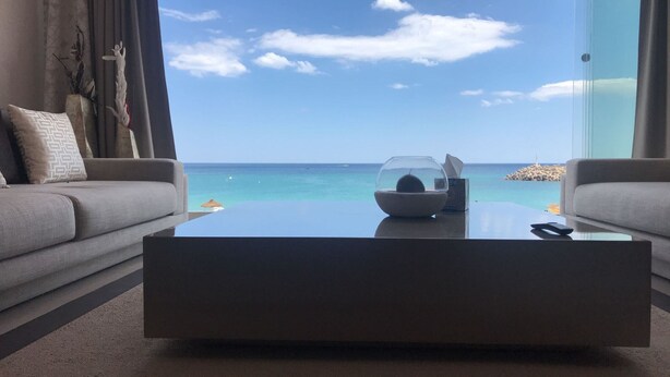 Een moderne woonkamer met een glazen salontafel, twee grijze banken en uitzicht op de oceaan.