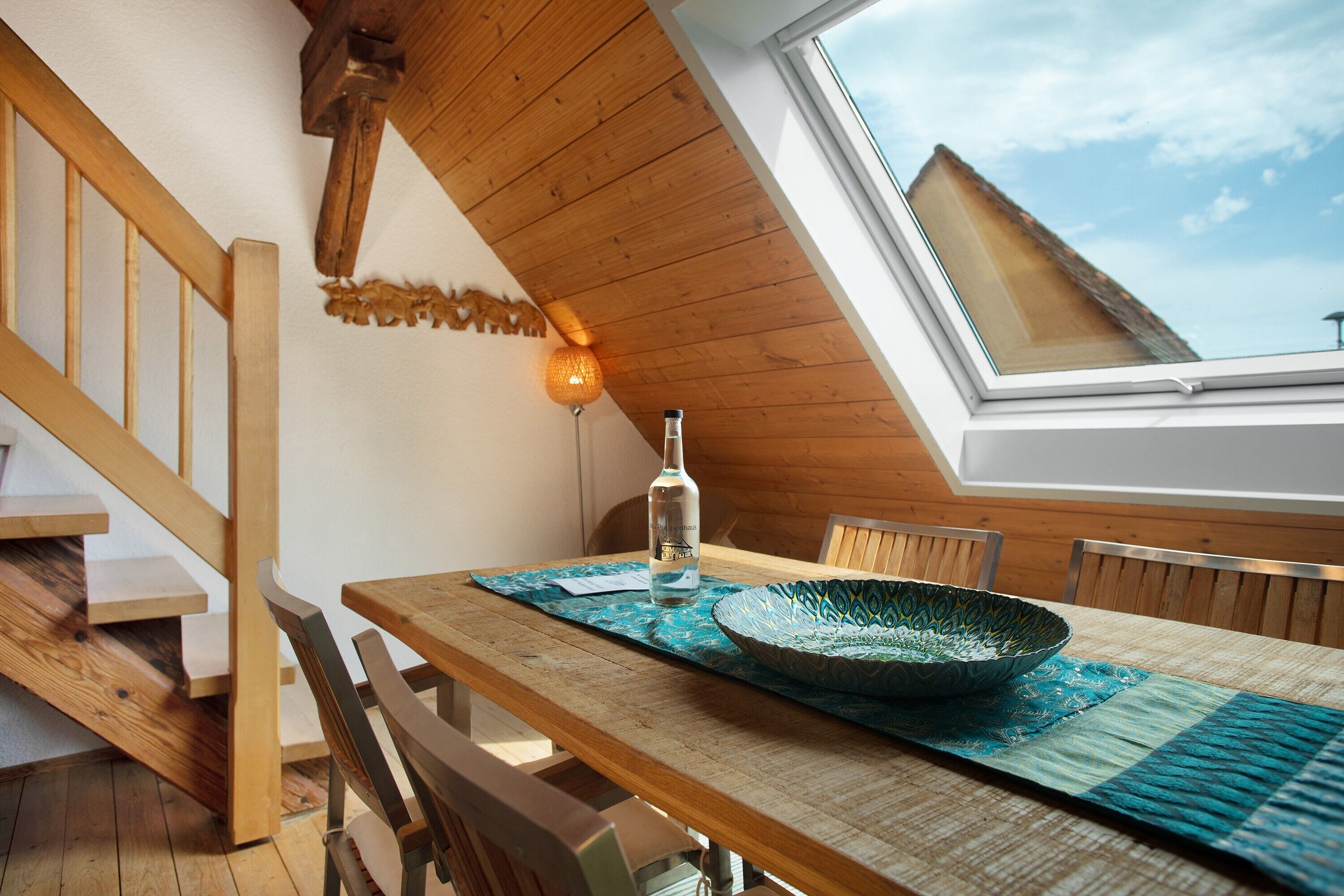 Een eethoek met een houten tafel, stoelen, een decoratieve schaal en een fles.