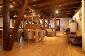 Ein rustikales Interieur mit sichtbaren Holzbalken, einem Essbereich mit Stühlen, einer Couch und einer Treppe.