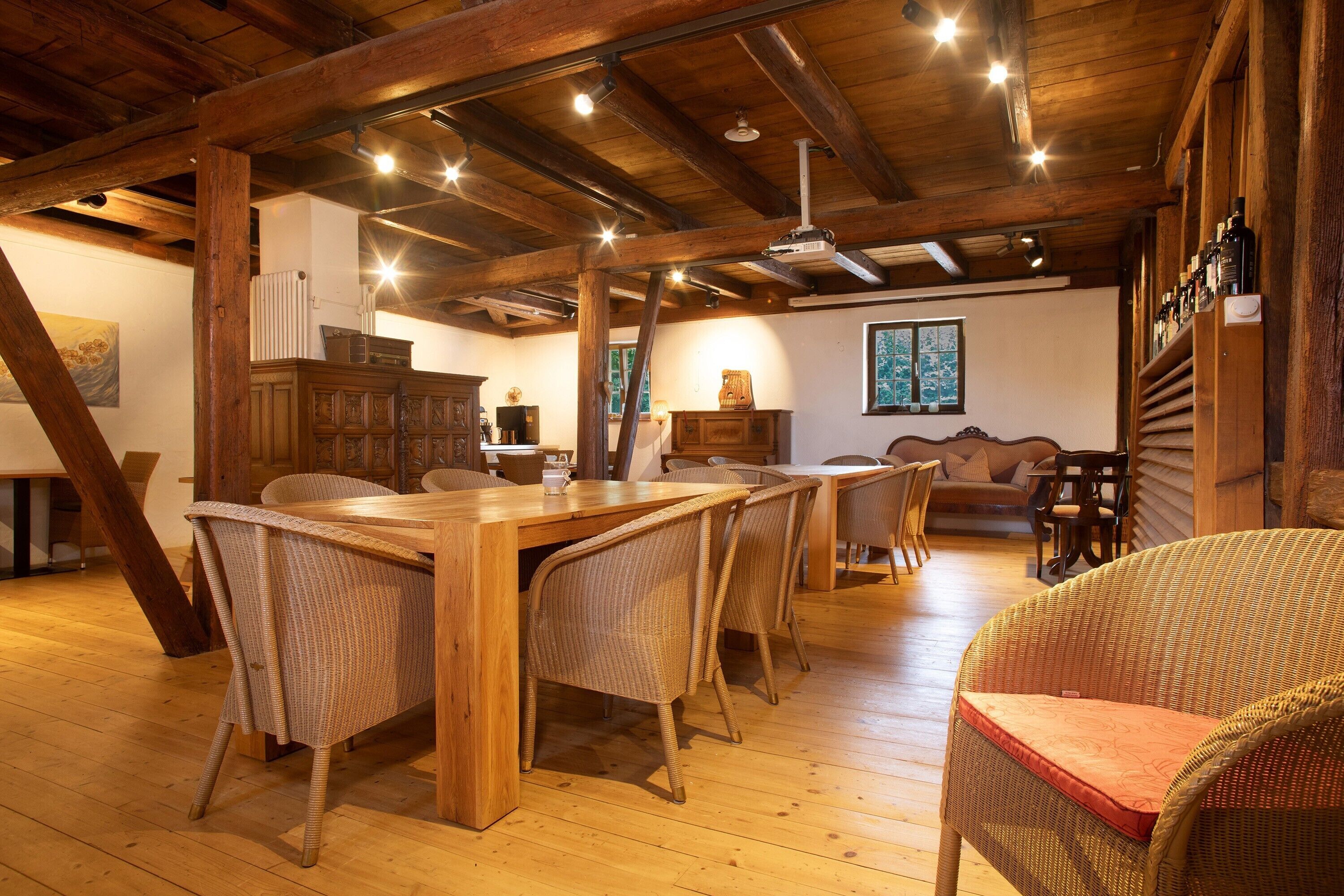 Un espace repas doté de meubles en bois, d’un plafond haut avec des poutres apparentes et d’un coin salon confortable avec des fauteuils en osier.