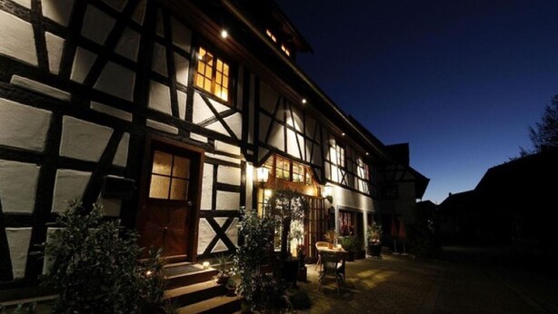 A traditional half-timbered building with a well-lit entrance and steps leading up to it. - Villa Puppenhaus – 'Apartment ehemalige Backstube' with Shared Terrace and Wi-Fi, Basement (Immenstaad am Bodensee)