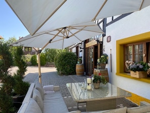 Un espace patio avec une table en verre, des coussins et un parasol blanc.