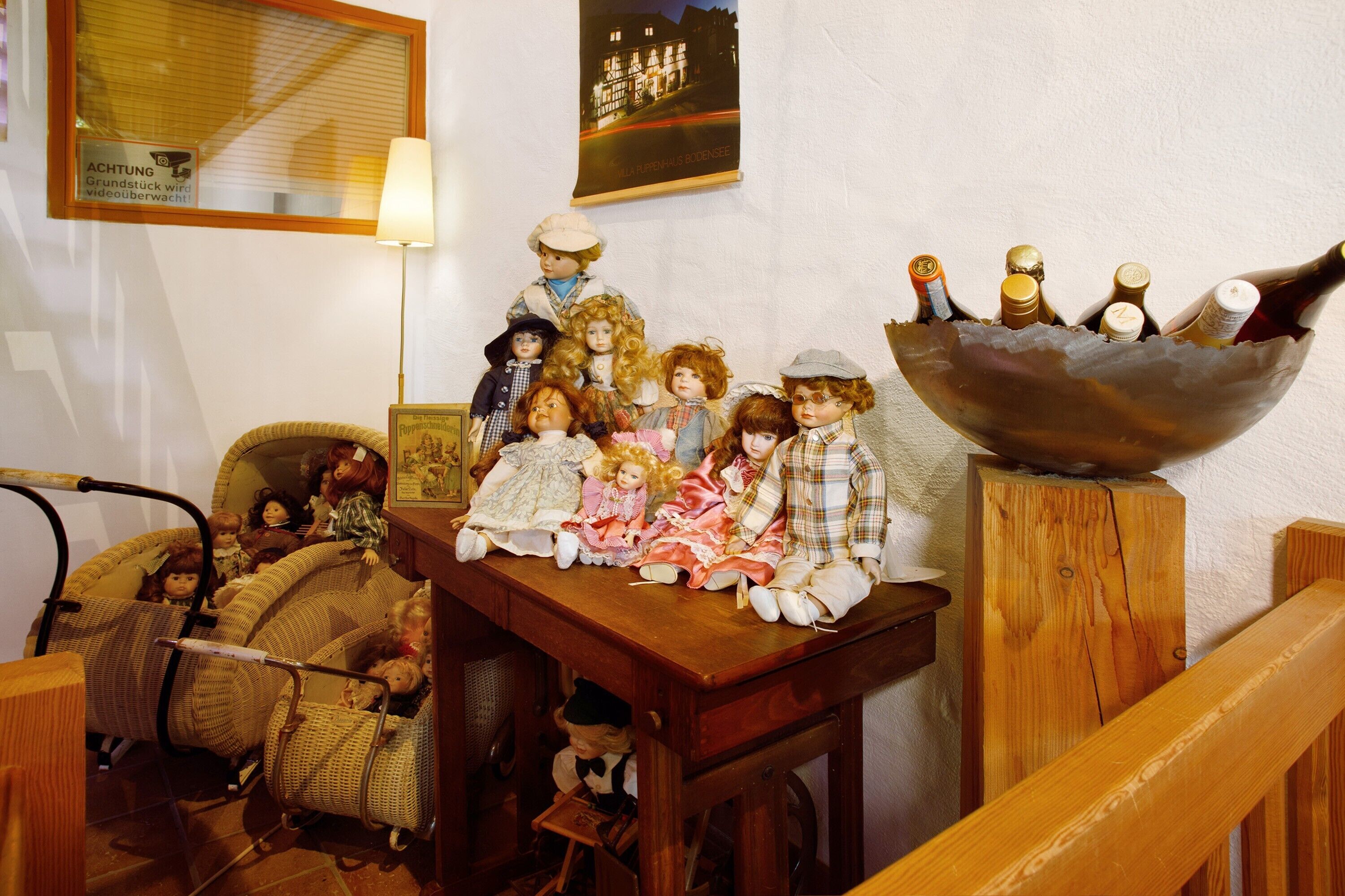 A room with a wooden table displaying dolls and a large metal bowl containing bottles.