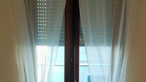 Une pièce dotée d’une porte-fenêtre coulissante, de rideaux blancs et légers, et offrant une vue sur un patio extérieur avec des chaises et une table en métal.