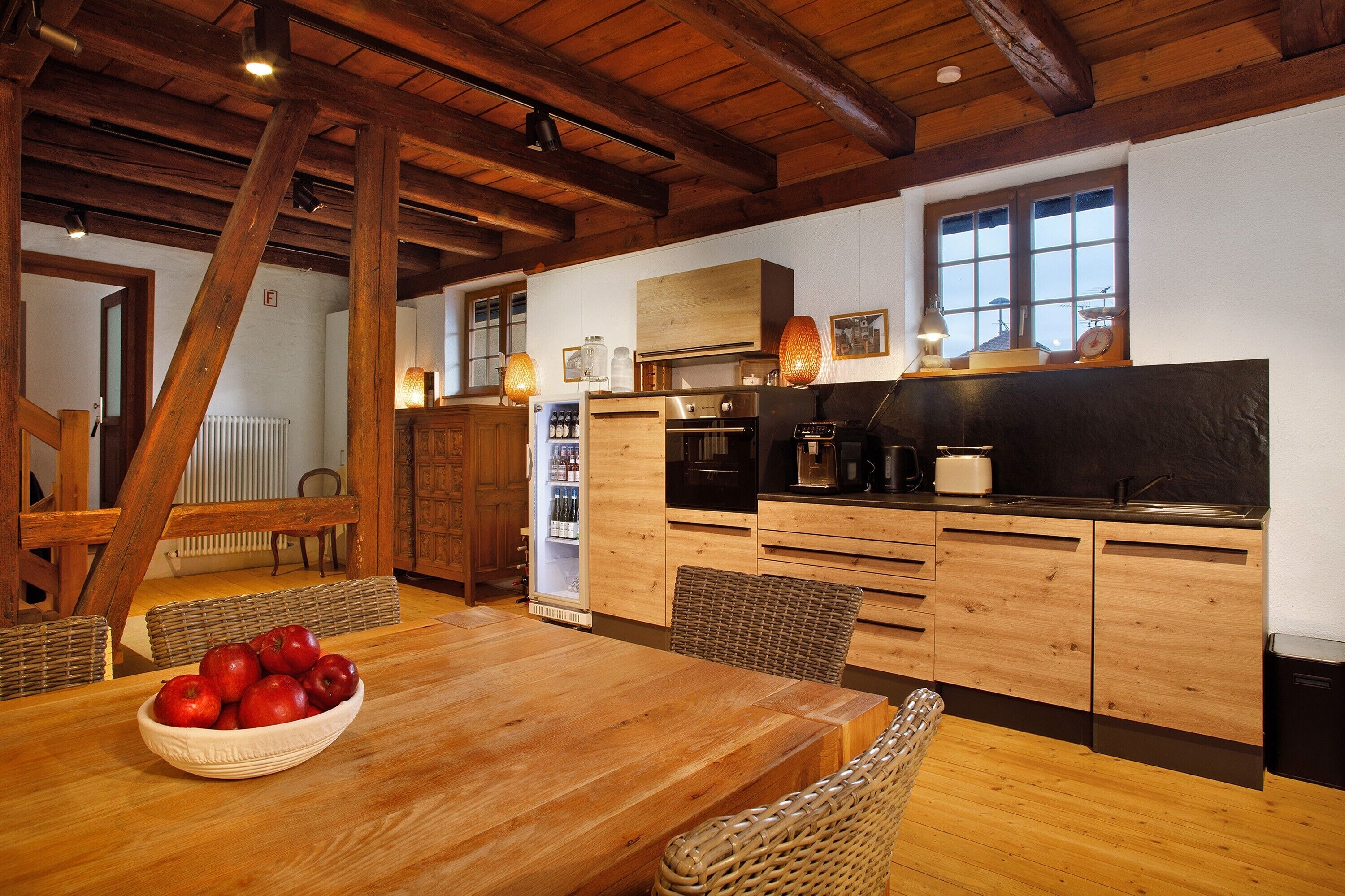 A wooden kitchen with a dining table, chairs, and a bowl of apples.
