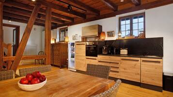 A wooden kitchen with a dining table, chairs, and a bowl of apples.
