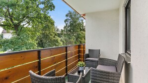 Ein Balkon mit Korbmöbeln, einer Topfpflanze und Blick auf Bäume und Gebäude.