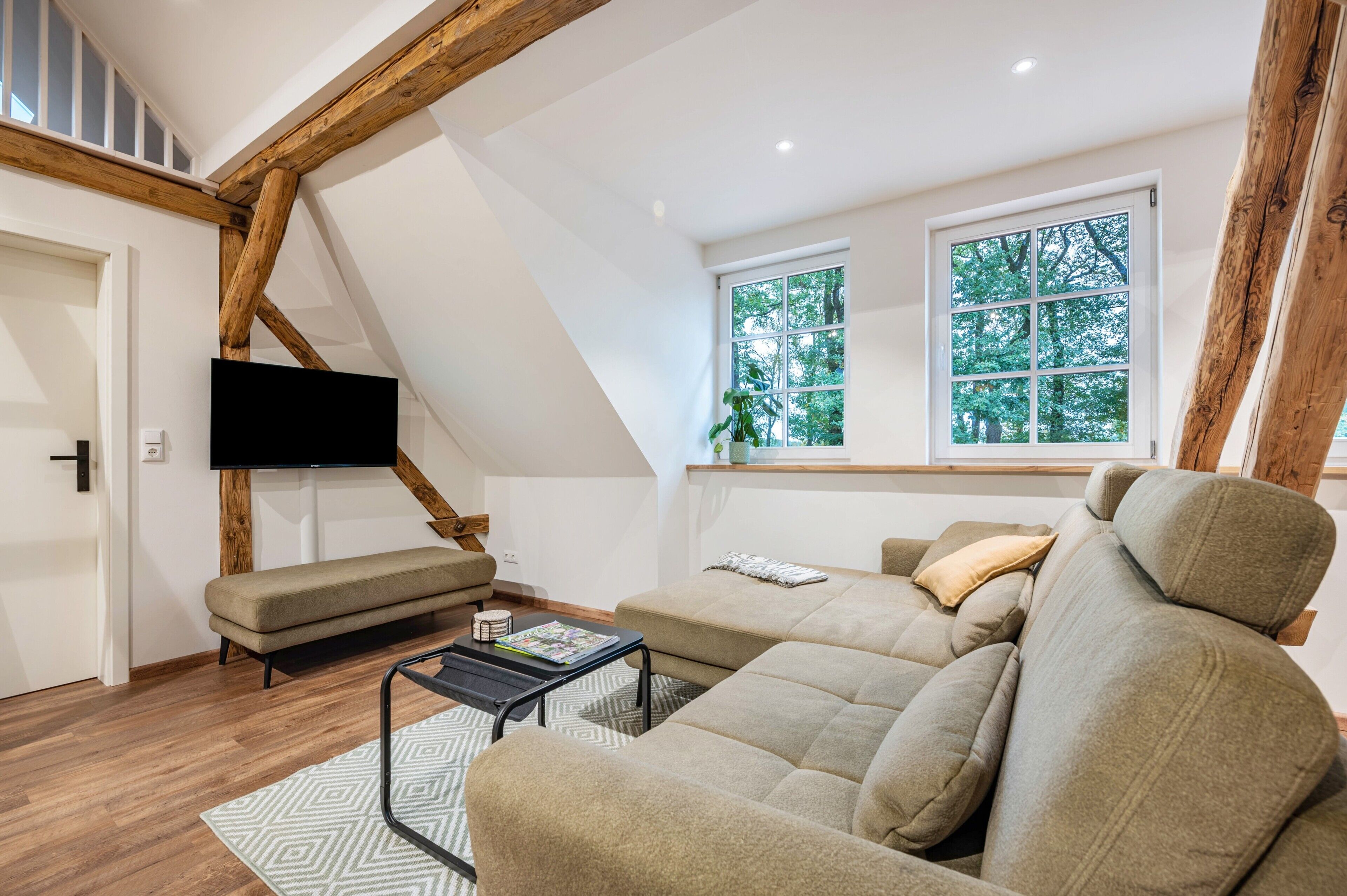 Ein modernes Wohnzimmer mit einem Ecksofa, einem Flachbildfernseher und einem Holzbalken an der Decke.