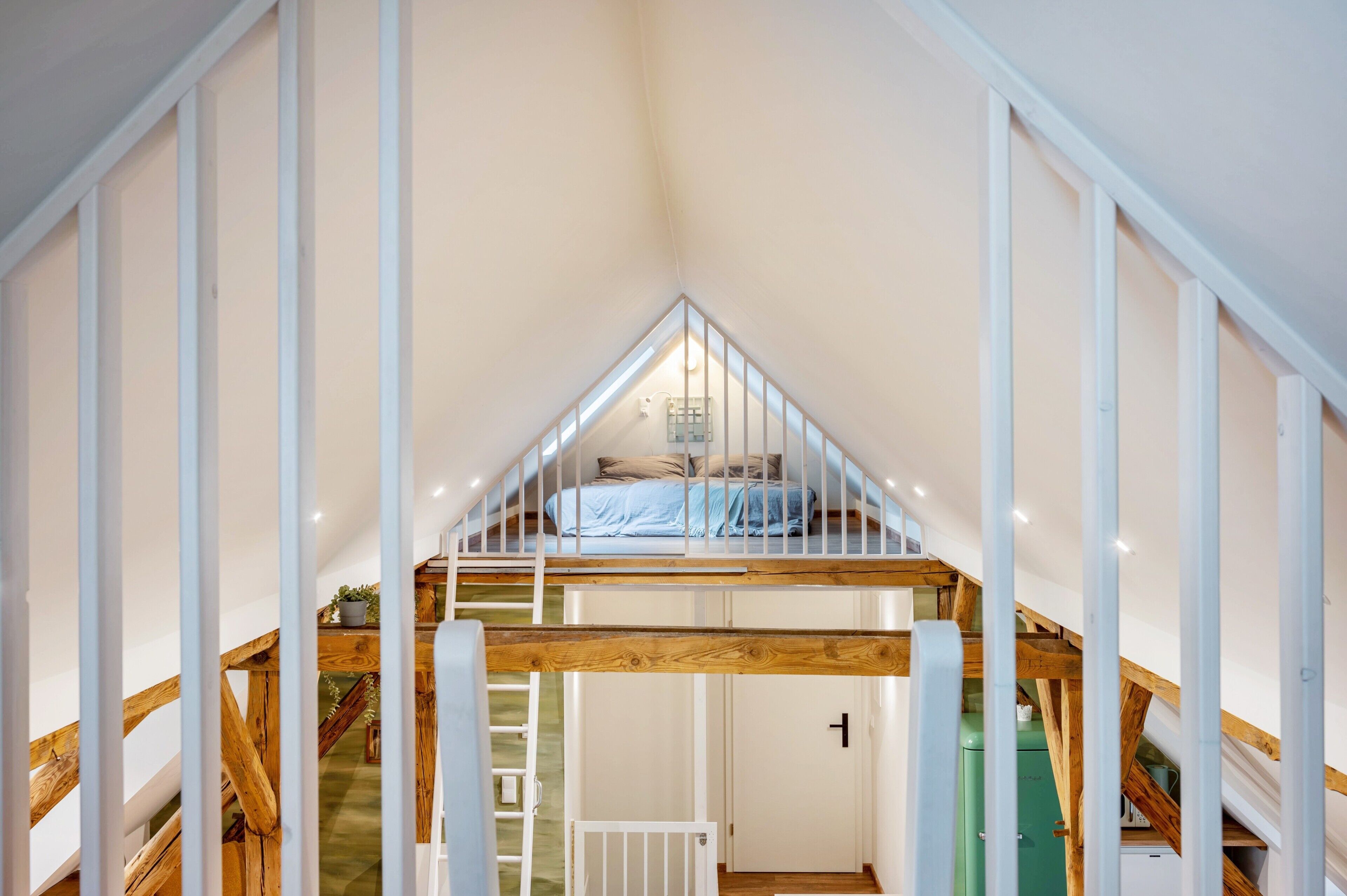 Ein Schlafzimmer im Loft-Stil mit schrägverlaufender Decke, einem Bett und einer Treppe, die zu einer erhöhten Ebene führt.