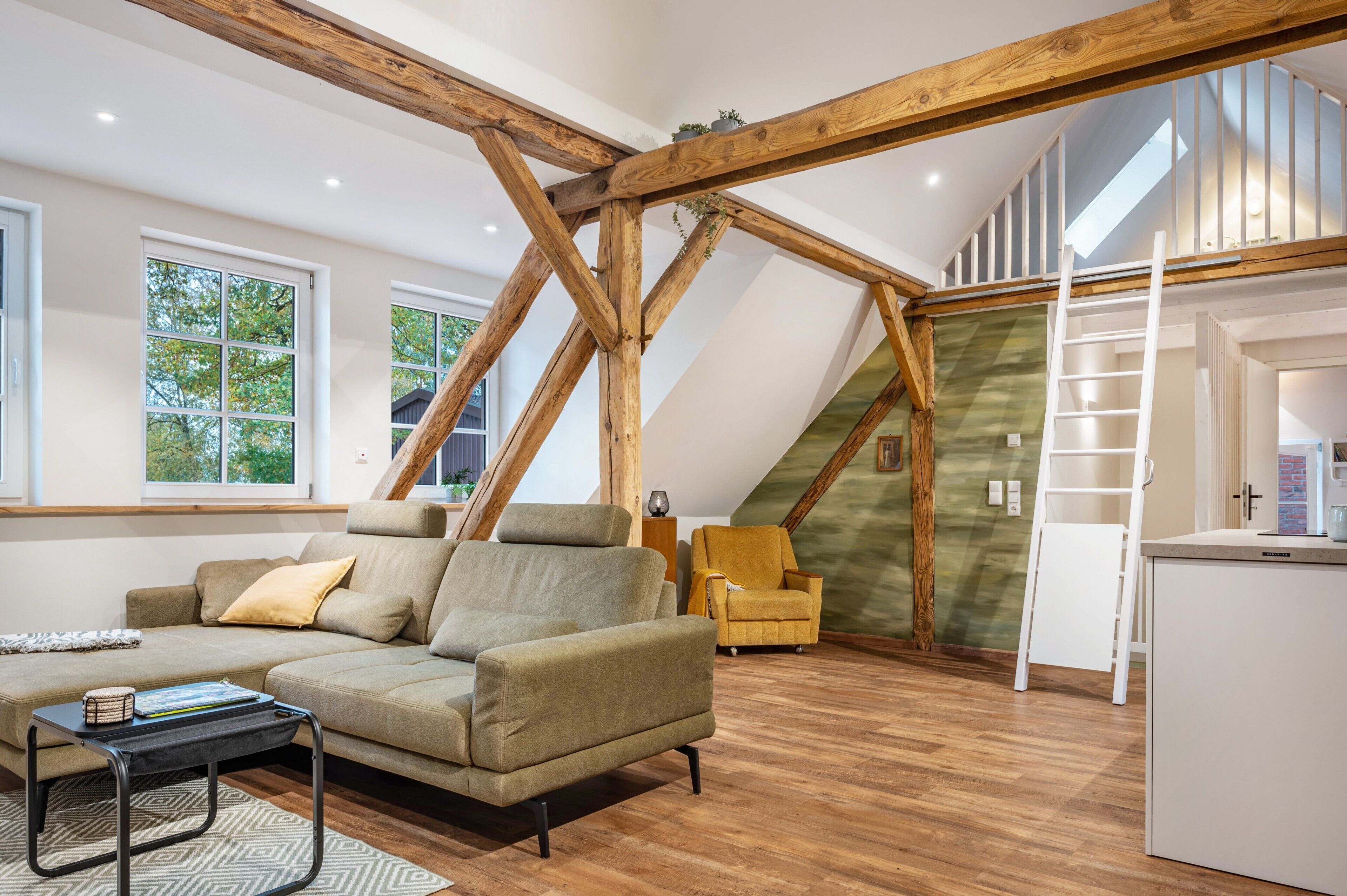 A loft-style room with a wooden beam ceiling, a sofa, a yellow armchair, a ladder, and a white cabinet.