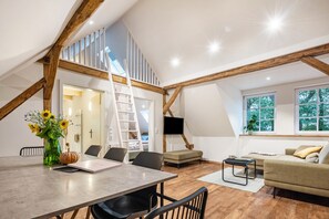 A loft-style room with a dining table, chairs, a sofa, a TV, and a staircase. - Holiday Apartment "Eichengeflüster Schwalbenloft" with a Private Terrace under the Oaks (Wagenfeld)