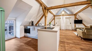 Un loft moderne comprenant une cuisine, un coin repas et un espace de vie, avec des poutres apparentes et une grande fenêtre.
