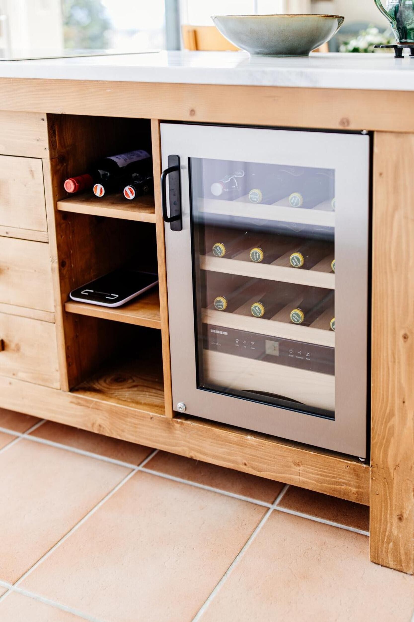 A wine refrigerator integrated into a wooden cabinet with wine bottles inside.