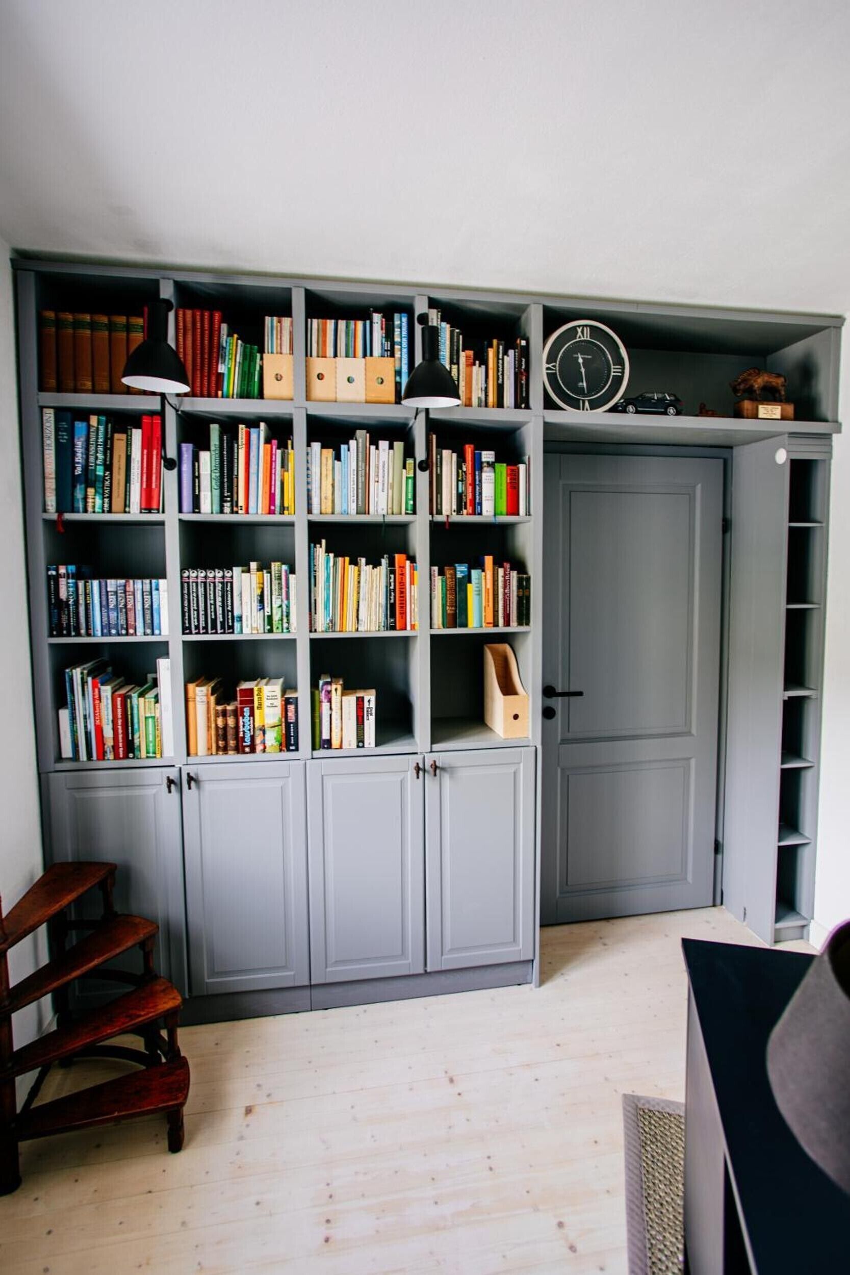 A room with a large grey bookshelf filled with books, a wooden chair, and a door.