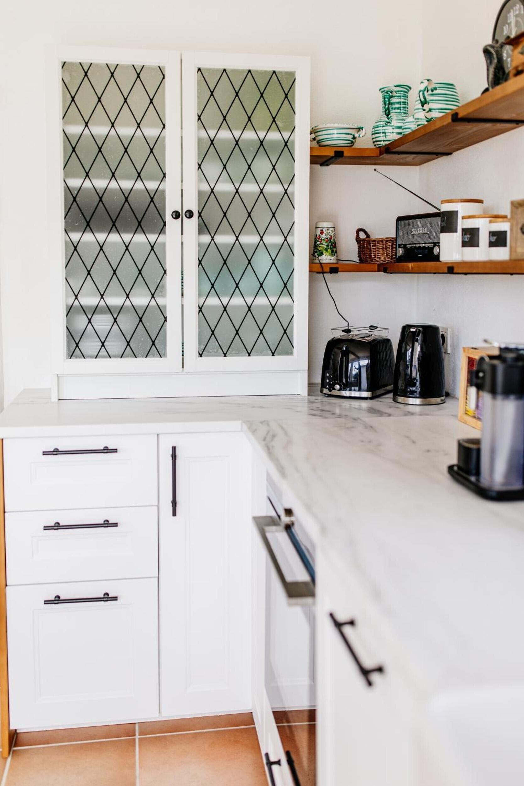A kitchen with white cabinets, a marble countertop, a coffee maker, a toaster, and a kettle.