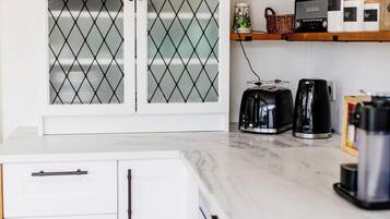 A kitchen with white cabinets, a marble countertop, a coffee maker, a toaster, and a kettle.