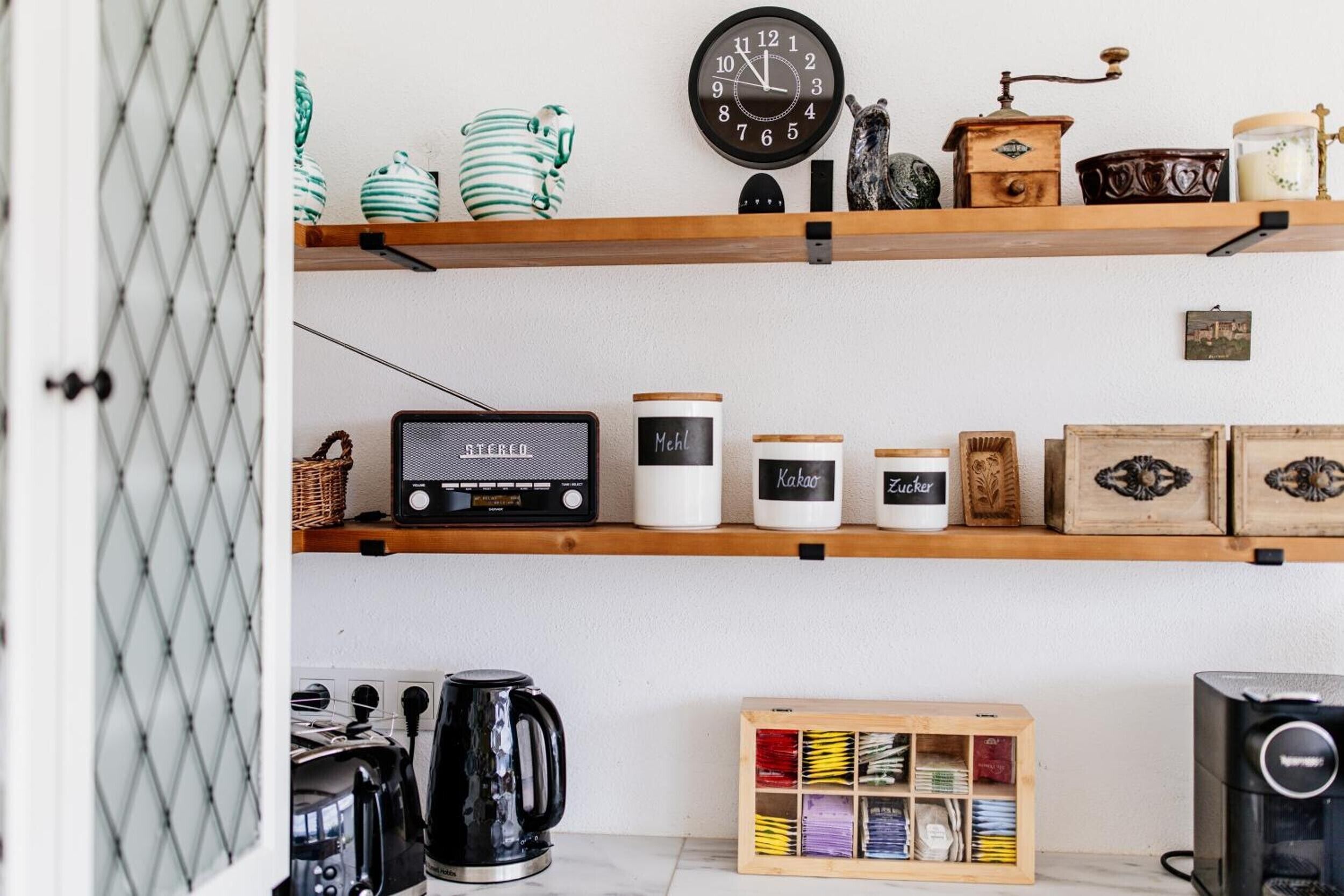A kitchen with a radio, shelves with jars, a coffee maker, and a wooden box with tea boxes.