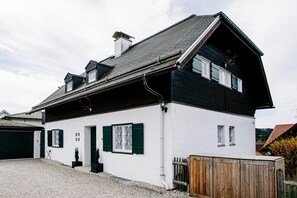 A two-story house with a white exterior and dark trim, a sloped roof, and a wooden fence in front.