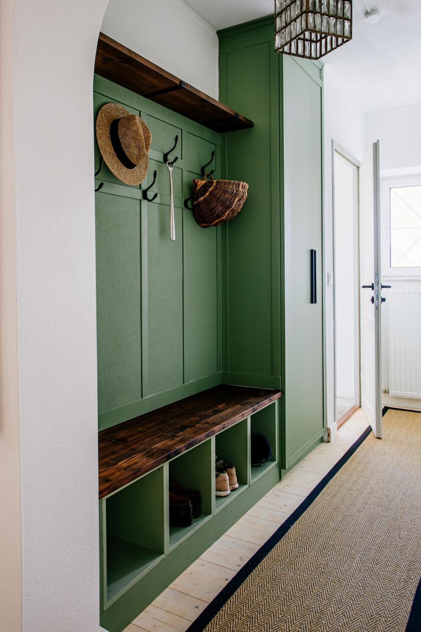 A green hallway with a bench, a hat rack, and a basket.