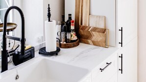 Ein modernes Badezimmer mit einem weißen Waschbecken, einem schwarzen Wasserhahn und einem Spiegel darüber. Auf der Arbeitsplatte liegen Holzschneidebretter und Flaschen.