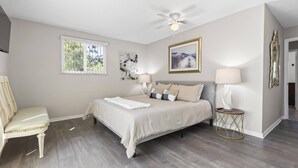 A bedroom with a bed, two bedside tables, a chair, a ceiling fan, and artwork on the walls. - Coral Paradise Golf Course Pool Home | Close To The Beach | Palm Coast | Dog Friendly (Palm Coast)
