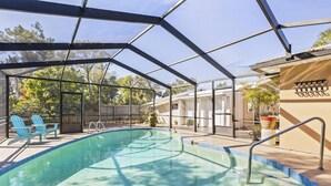 A covered swimming pool with blue chairs and a ladder, surrounded by a fence and trees. - Coral Paradise Golf Course Pool Home | Close To The Beach | Palm Coast | Dog Friendly (Palm Coast)