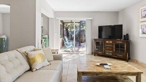 A living room with a sofa, a coffee table, a TV, and a cabinet. There is a glass door leading to an outdoor area with plants. - Coral Paradise Golf Course Pool Home | Close To The Beach | Palm Coast | Dog Friendly (Palm Coast)