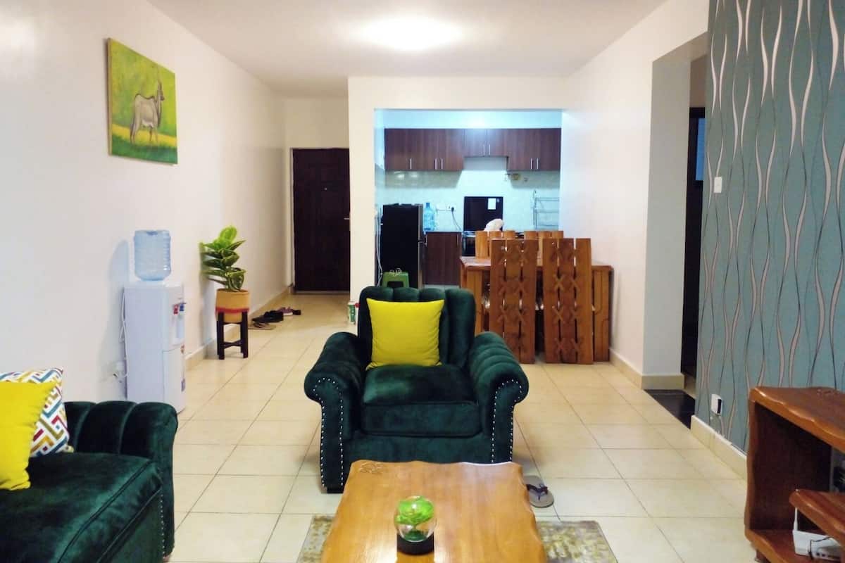 A living room with a green sofa, a wooden coffee table, and a dining area with wooden chairs and a table.