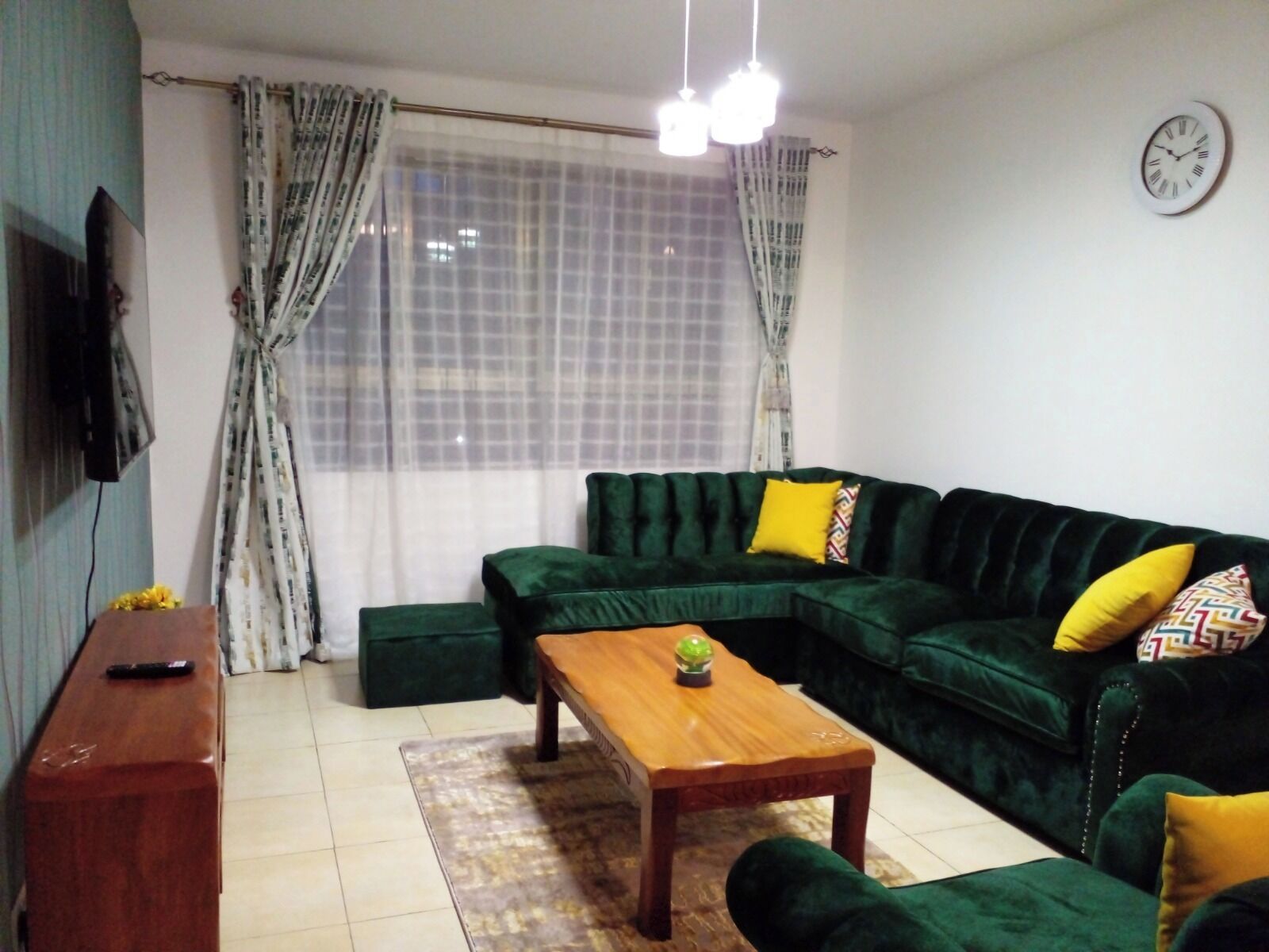 Una sala de estar con un sofá verde, una mesa de centro de madera y un televisor en la pared.