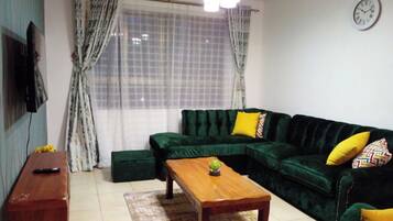 Una sala de estar con un sofá verde, una mesa de centro de madera y un televisor en la pared.