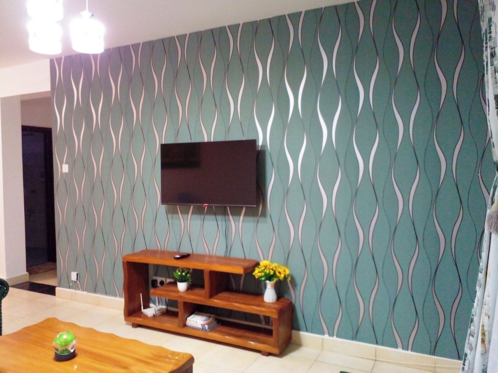 A living room with a patterned wall, a flat-screen TV mounted above a wooden entertainment unit, and a coffee table with a decorative item.