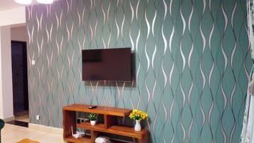 A living room with a patterned wall, a flat-screen TV mounted above a wooden entertainment unit, and a coffee table with a decorative item.