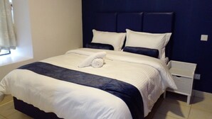 Una cama bien hecha con ropa de cama blanca y azul marino, una mesita de noche blanca y un cabecero azul oscuro.