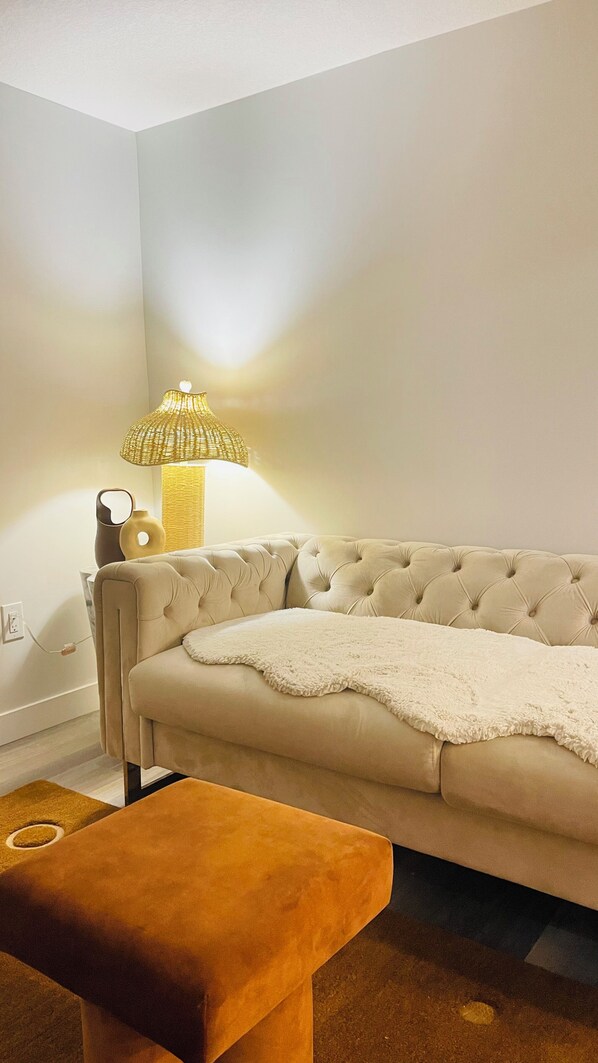 Una sala de estar con un sofá beige, un otoman marrón y una lámpara con pantalla de mimbre.