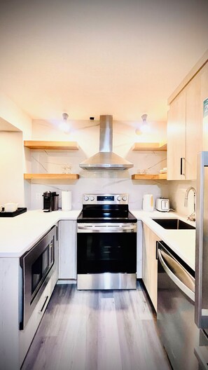 A modern kitchen with a stainless steel range hood, a built-in oven, a microwave, and a sink.