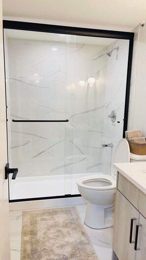 A modern bathroom with a glass-enclosed shower, a toilet, and a sink with a basket of towels.