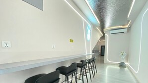 A modern bar area with a long counter, black bar stools, and a ceiling with a textured pattern. - U Capsule Hotel  (Kulai)