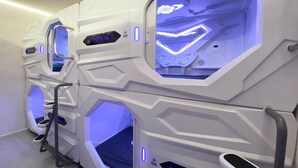 A row of hexagonal massage pods with illuminated interiors, each pod featuring a control panel and a small window. - U Capsule Hotel  (Kulai)