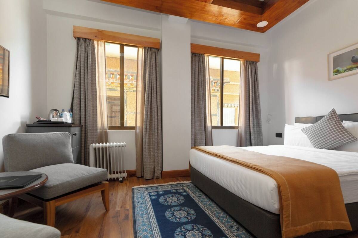 A hotel room with a bed, a chair, a desk, and a radiator.