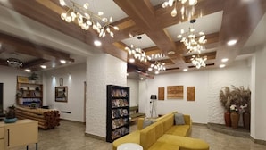 A modern lobby with a yellow sectional sofa, a small round table, and a bookshelf. - Hotel Dralha  (Thimphu)