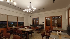 A restaurant with wooden tables and chairs, a chandelier, and large windows with views. - Hotel Dralha  (Thimphu)