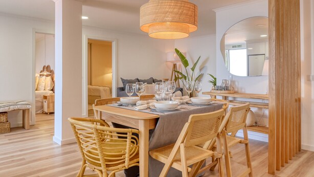 A dining area with a wooden table set for four, surrounded by wicker chairs. A woven pendant light hangs above the table, and there is a mirror on the wall to the right. - Vale dos Amores, a Home in Madeira (Calheta)