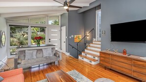 A spacious living room with hardwood floors, a grey sofa, a red armchair, a wooden coffee table, and a staircase leading to another level. - Charming 3-bedroom house with spacious backyard in enjoyable Charlotte.  (Charlotte)